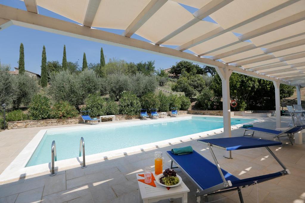 a swimming pool with two blue chairs and a pergola at Henry House in Cinigiano
