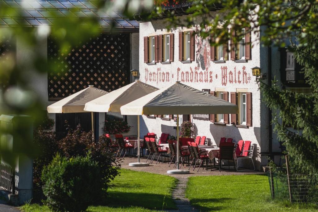 a patio with chairs and umbrellas in front of a building at Walch's Camping & Landhaus in Braz