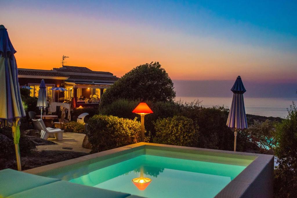 a swimming pool with a sunset in the background at Bajaloglia Resort in Castelsardo