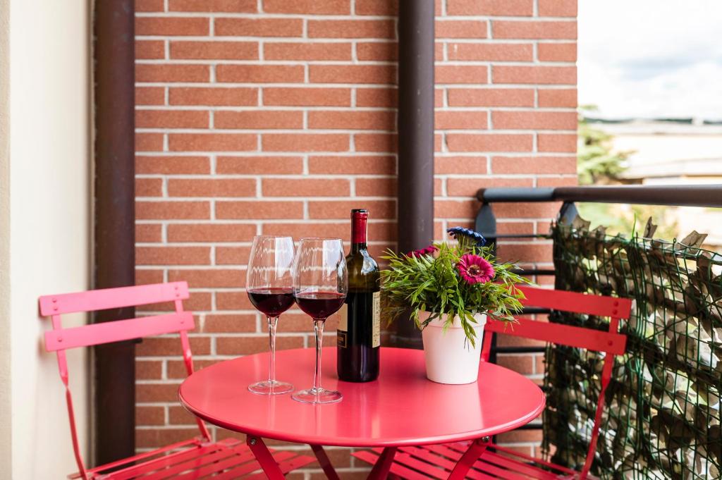 a red table with two glasses of wine and a plant at Hostly - Family Home Strada dell'Olio - Brand new 2BR, 2 Bathrooms with AC in Cascina