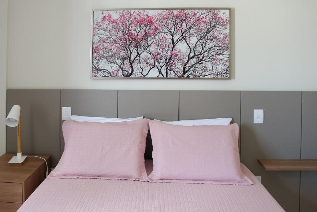 Una cama con almohadas rosas y una pintura encima. en FANTÁSTICO APARTAMENTO NA BARRA en Salvador