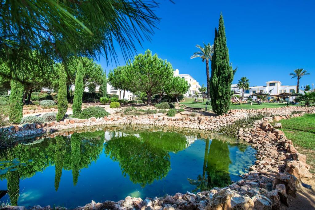 a pond in a park with trees and buildings at Vale d'El Rei Hotel & Villas in Carvoeiro