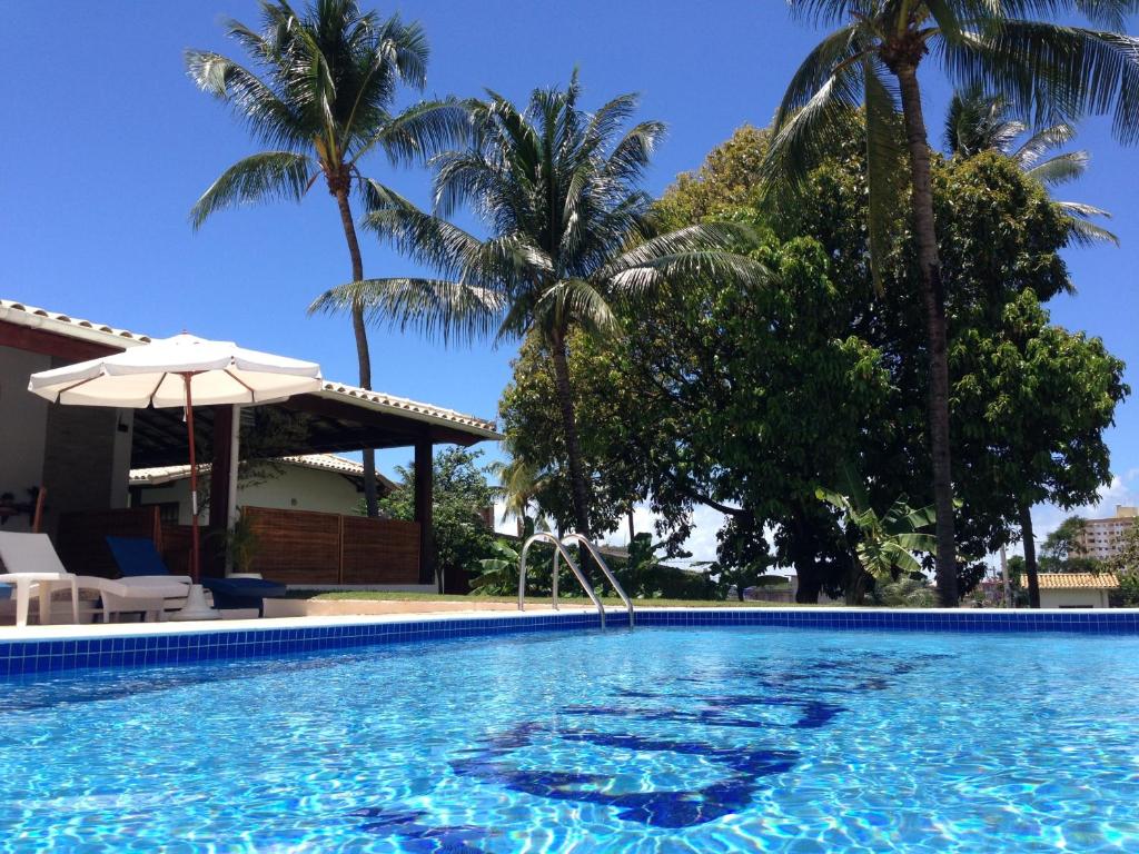 una piscina con palmeras y una sombrilla en Hotel Pousada Salvador Paradise, en Lauro de Freitas