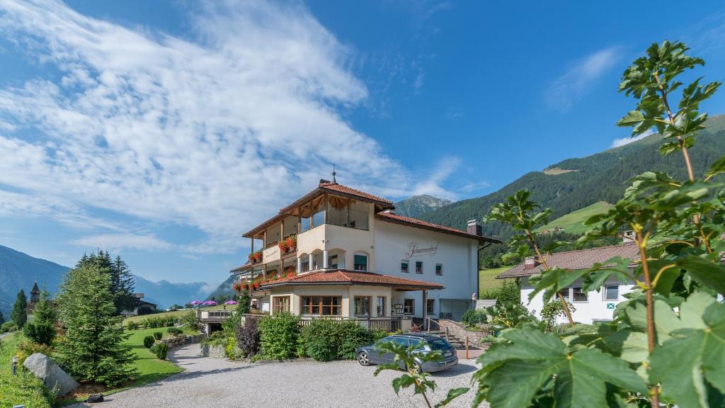 uma casa numa colina com montanhas ao fundo em Berghotel Johanneshof em Anterselva di Mezzo