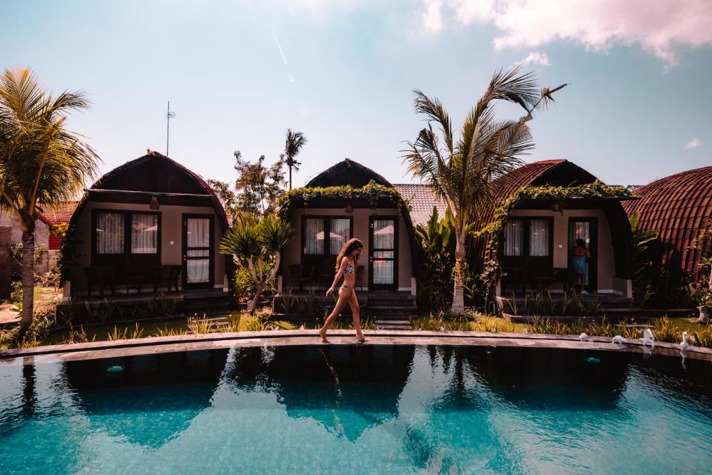 a woman walking across a pool in front of a house at Papa Sun Villas in Nusa Penida