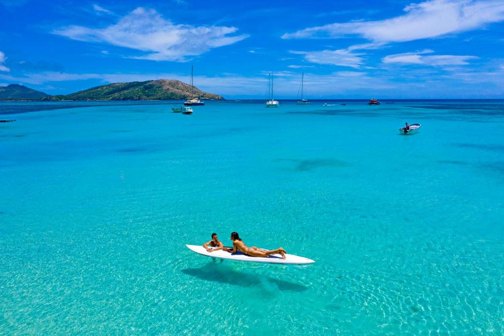 zwei Leute sitzen auf einem Surfbrett im Wasser in der Unterkunft Oarsman's Bay Lodge in Nacula Island