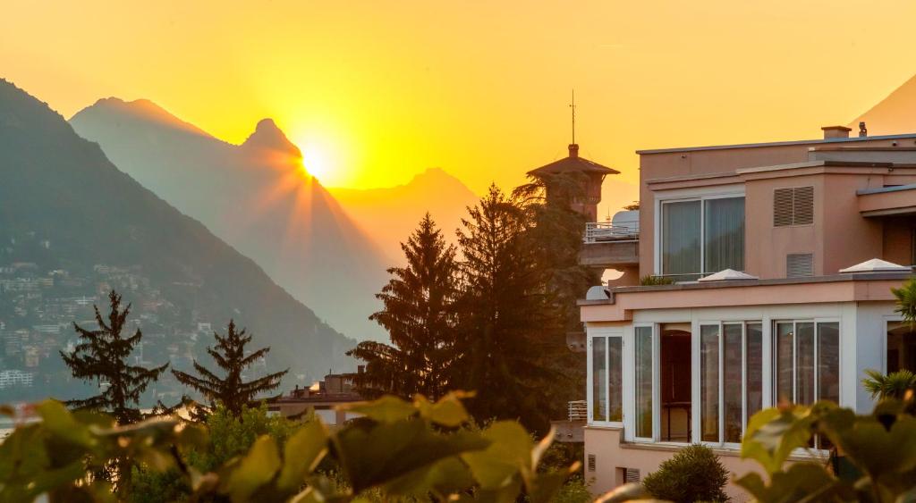 a house with the sun setting behind a mountain at Suitenhotel Parco Paradiso in Lugano