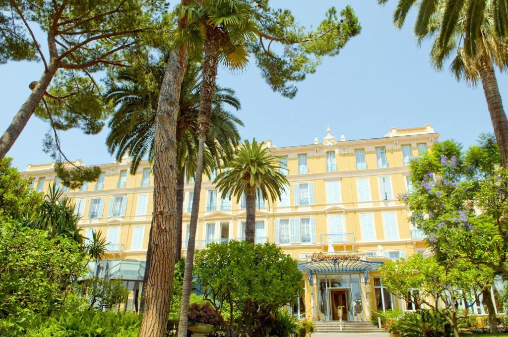 a building with palm trees in front of it at Hôtel Miléade L'Orangeraie - Menton in Menton