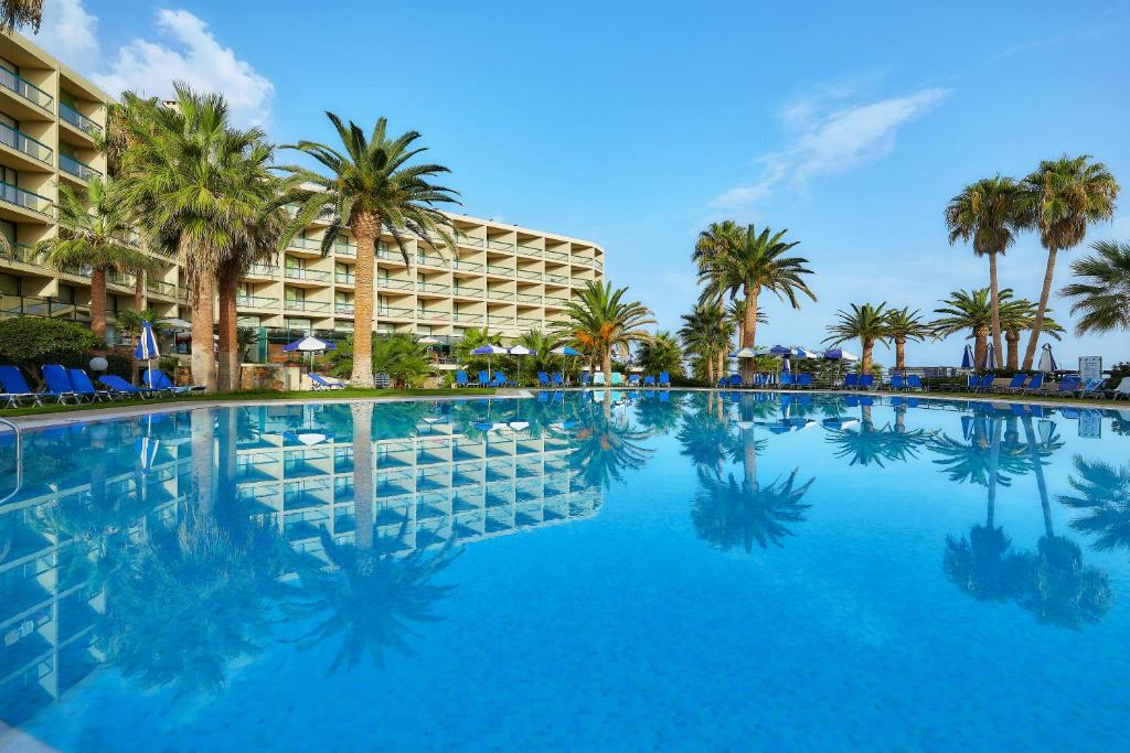 een groot zwembad met palmbomen en een hotel bij Sirens Beach & Village in Malia