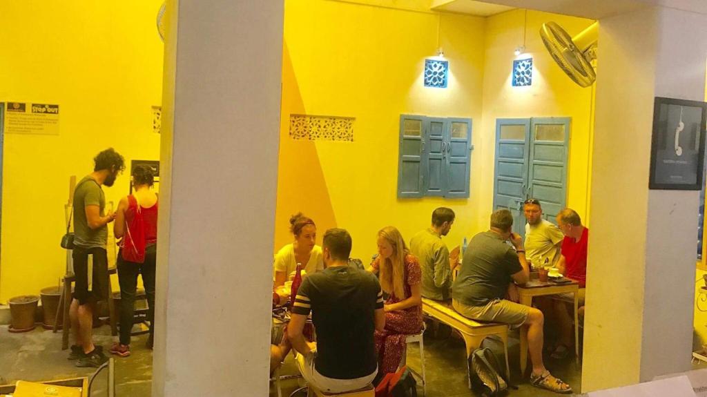 a group of people sitting at tables in a yellow room at Housetel in Jaipur