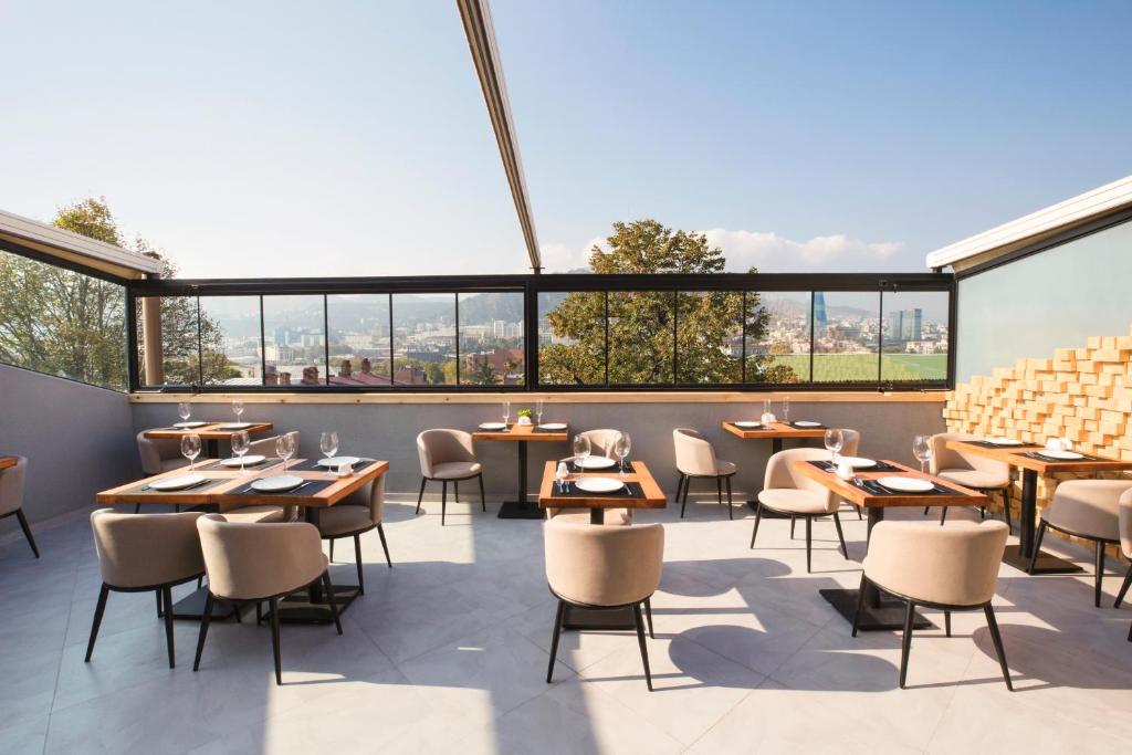 un restaurante con mesas, sillas y ventanas grandes en Ornament Boutique Hotel en Tiflis