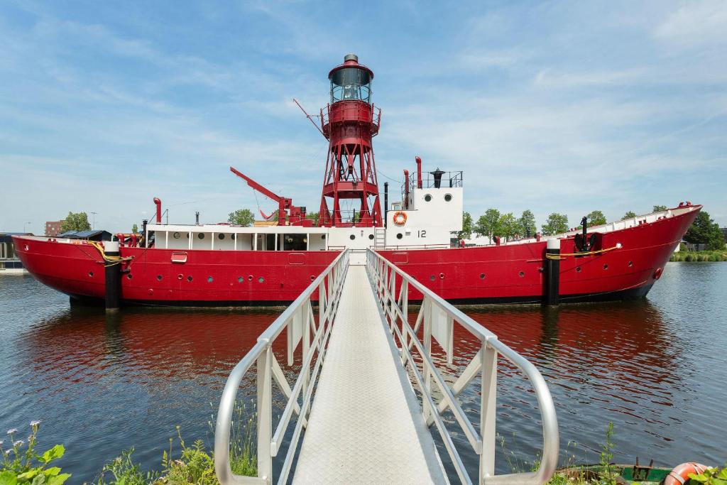 a red boat in the water next to a lighthouse at Lightship Amsterdam in Amsterdam