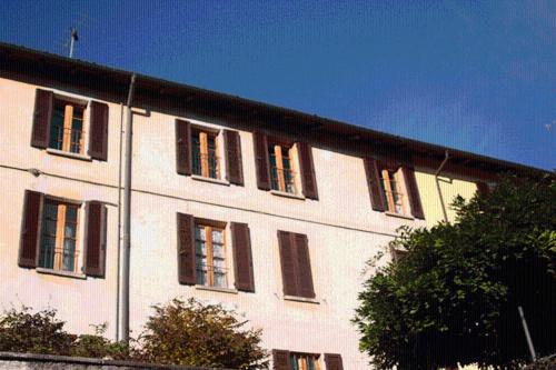 un grande edificio bianco con finestre con persiane nere di Le Camelie a Brissago Valtravaglia