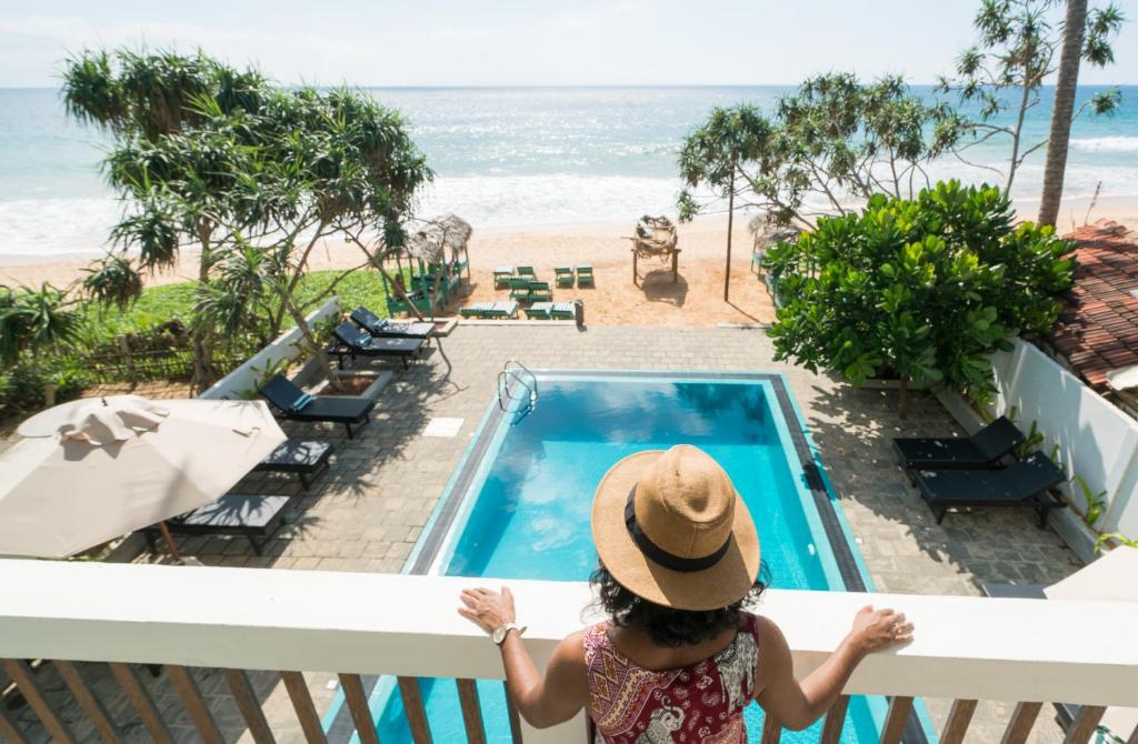 una mujer sentada en un balcón con vistas a la playa en At Ease Beach Hotel, en Hikkaduwa