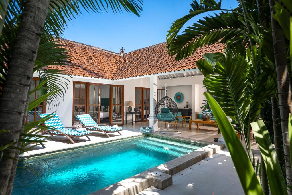 a swimming pool with chairs and a house at Villa Merah in Seminyak