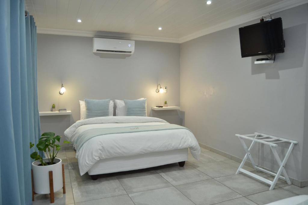 a white bedroom with a bed and a tv at African Sands Guesthouse LOAD SHEDDING FREE in Bloemfontein