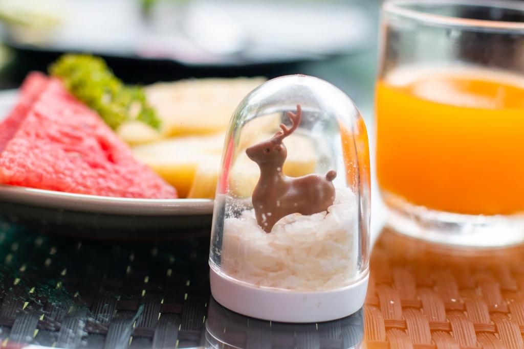 A close-up breakfast setting with fruit, orange juice and a decorative rabbit under a glass dome.