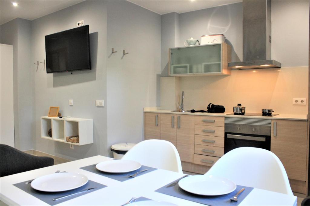 TV y cocina con mesa y sillas blancas. en Alguera Hola Apartments, en Barcelona