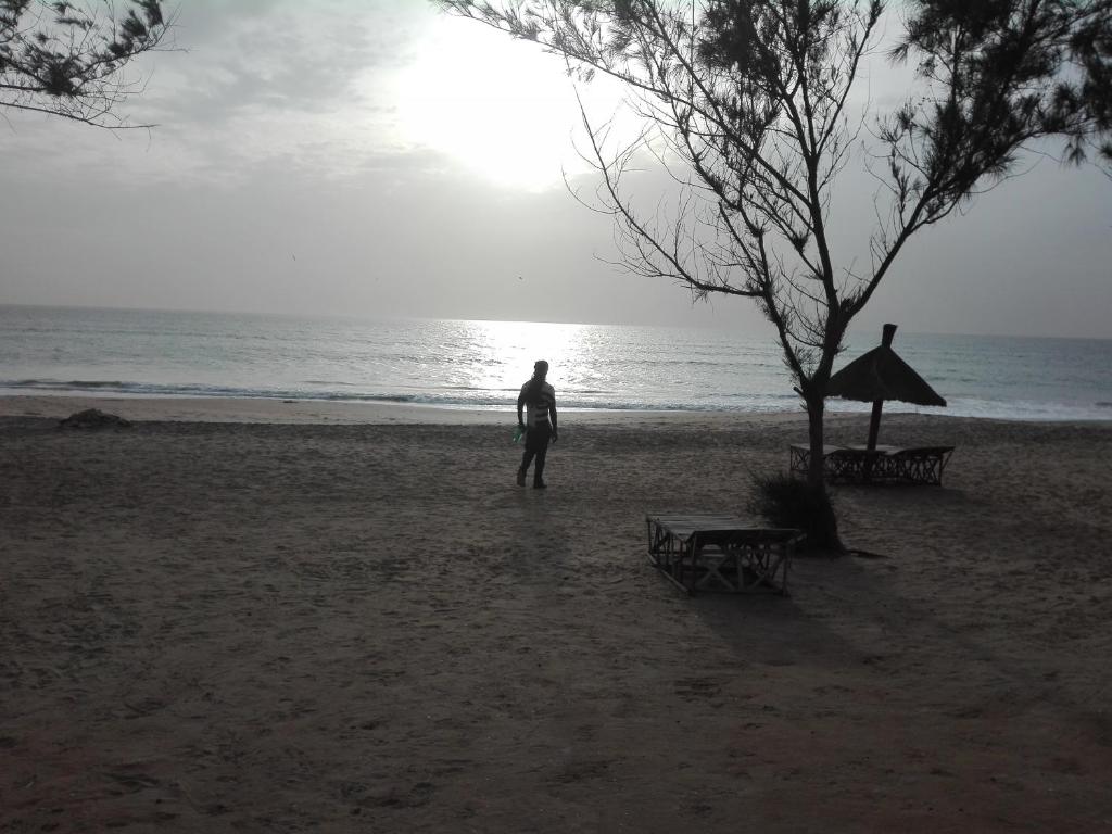 un hombre parado en una playa cerca del océano en Chez medzo et patou, en Poponguine
