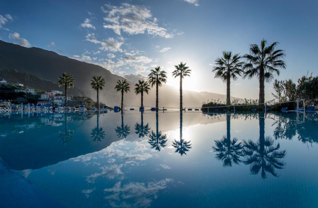 a pool of water with palm trees and mountains at Monte Mar Palace Hotel in Ponta Delgada
