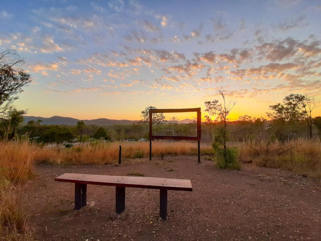 a bench in a field with the sunset in the background at Mt Larcom Tourist Park in Mount Larcom
