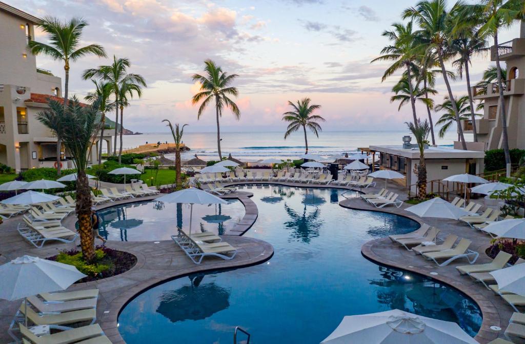 a resort pool with chairs and palm trees and the ocean at Pueblo Bonito Mazatlan Beach Resort - All Inclusive in Mazatlán