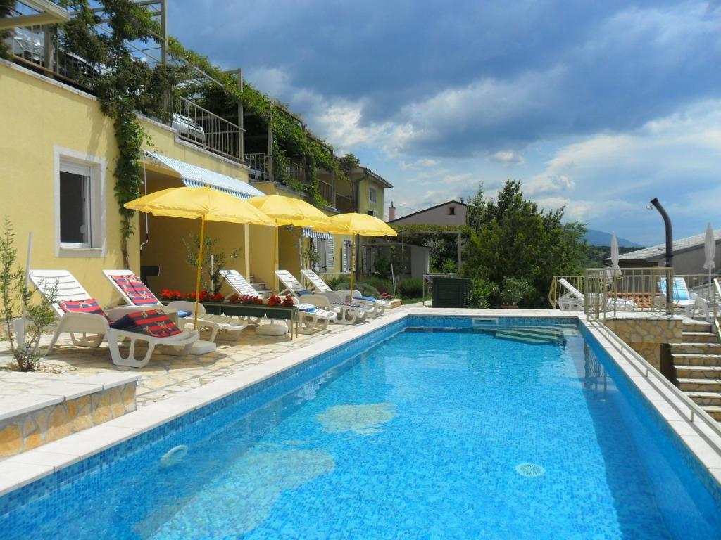 a swimming pool with chairs and umbrellas next to a building at Apartments Zlato - with pool in Senj