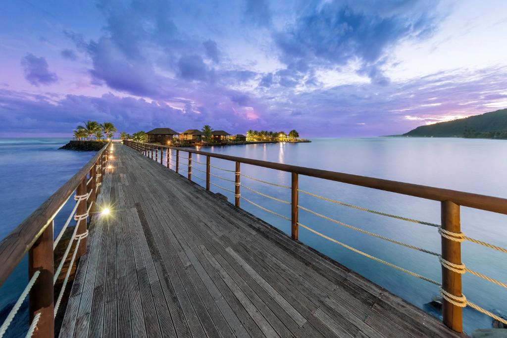 a wooden pier stretches out into the water at sunset at Aga Reef Resort and Spa in Lalomanu