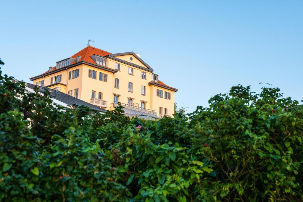 un bâtiment jaune avec un toit rouge derrière quelques arbres dans l'établissement Hotel Bretagne, à Hornbæk