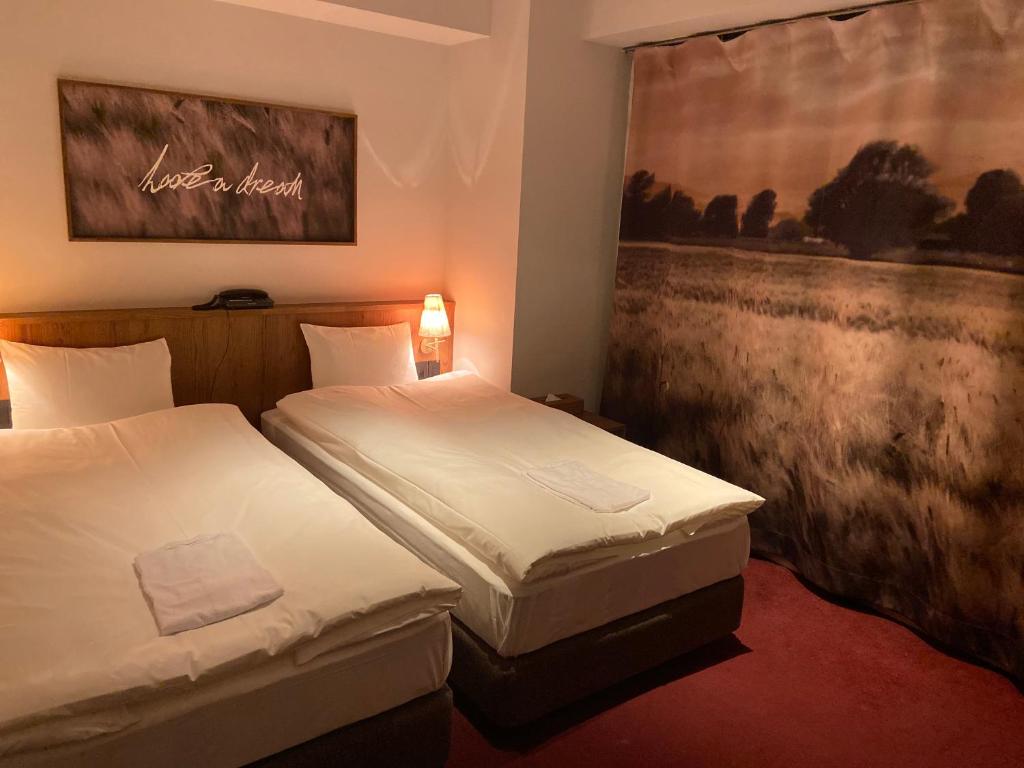 two beds in a hotel room with a painting on the wall at The Wall Hotel in Osaka