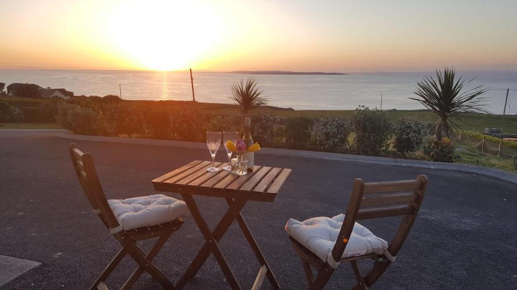 einem Holztisch mit zwei Stühlen mit Blick auf den Sonnenuntergang im Hintergrund in der Unterkunft Blue Ocean Guest Suites in Doolin