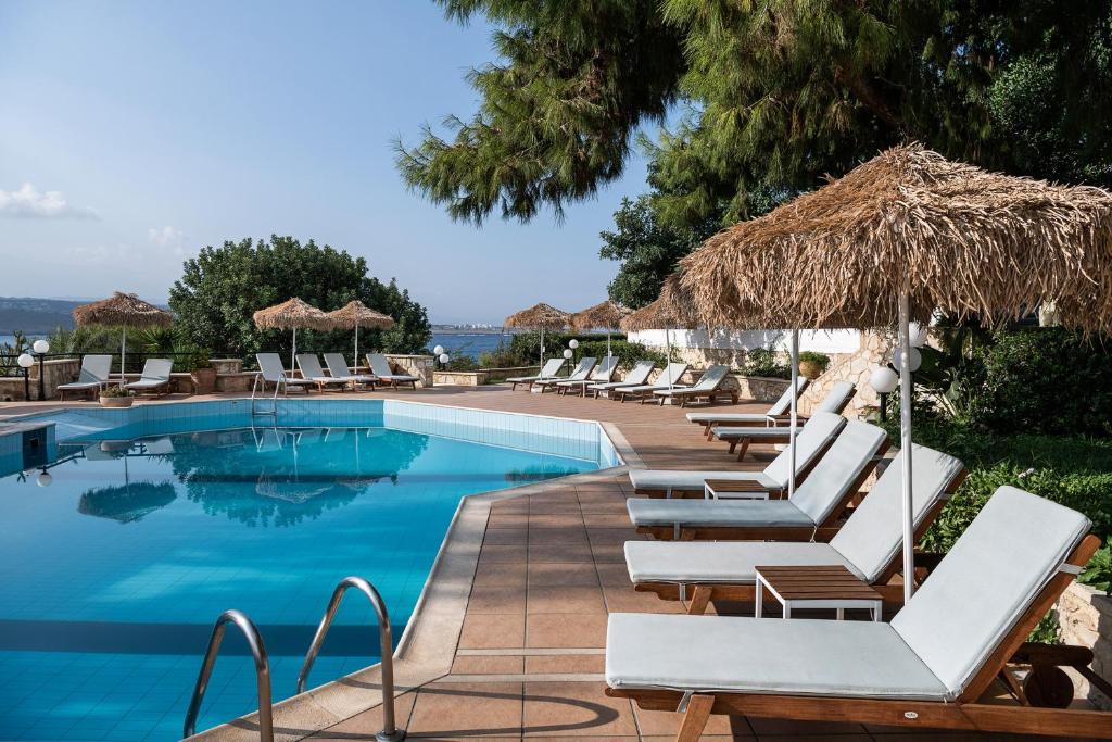 una piscina con sedie a sdraio e ombrellone di paglia di Alianthos Suites a Tersanas