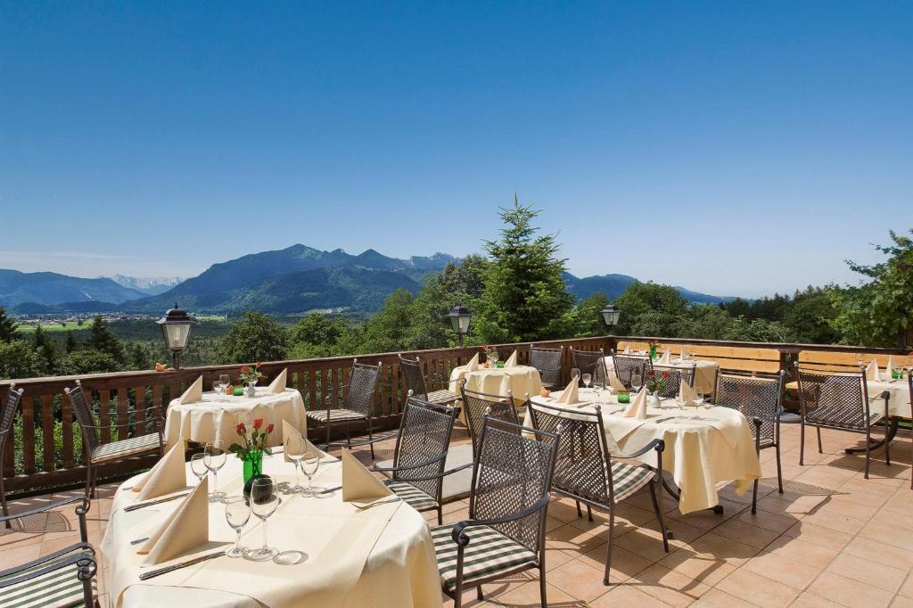 un restaurante con mesas y sillas con montañas al fondo en Hotel Restaurant Ferienwohnungen ALPENHOF en Übersee