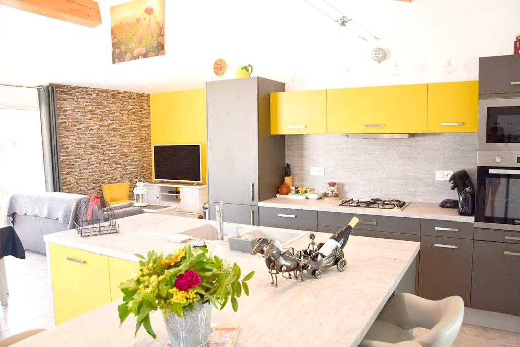 una cocina con armarios amarillos y una mesa con un jarrón de flores en Maison de 4 chambres avec piscine privee jardin amenage et wifi a La Roche sur le Buis, en La Roche-sur-le-Buis