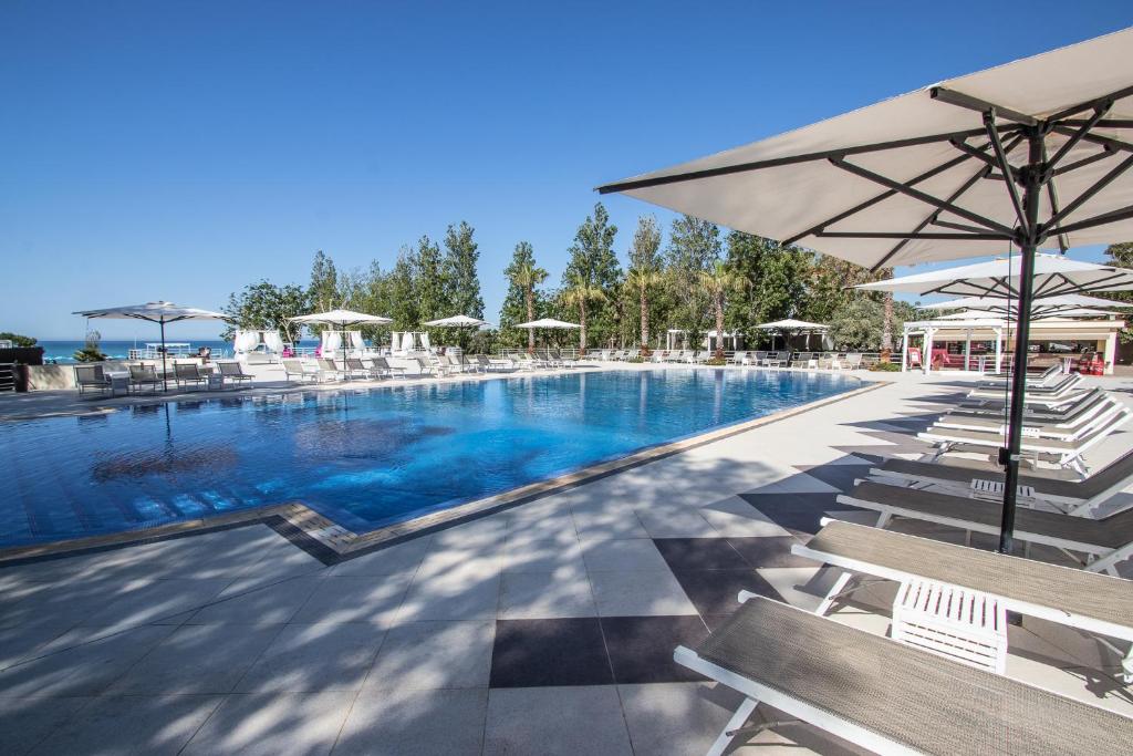 una gran piscina con sillas y sombrilla en Le Dune Resort, en Menfi