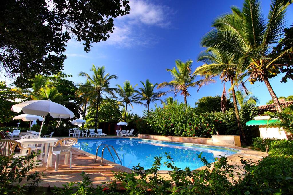 una piscina con sillas, sombrilla y palmeras en Canto d Alvorada Hotel Pousada, en Arraial d'Ajuda