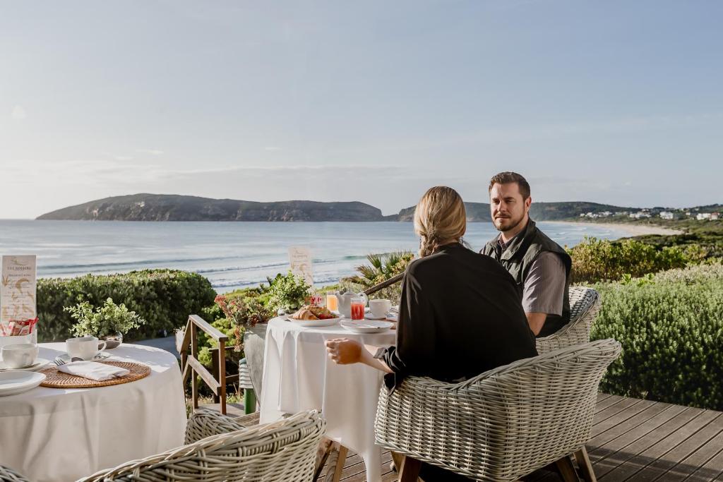 a man and woman sitting at a table overlooking the ocean at The Robberg Beach Lodge - Lion Roars Hotels & Lodges in Plettenberg Bay