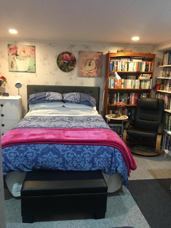 a bedroom with a bed and a chair and bookshelves at Sharyn’s B & B in Dunedin