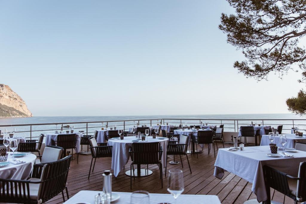 a restaurant with white tables and chairs and the ocean at Hôtel Les Roches Blanches Cassis in Cassis