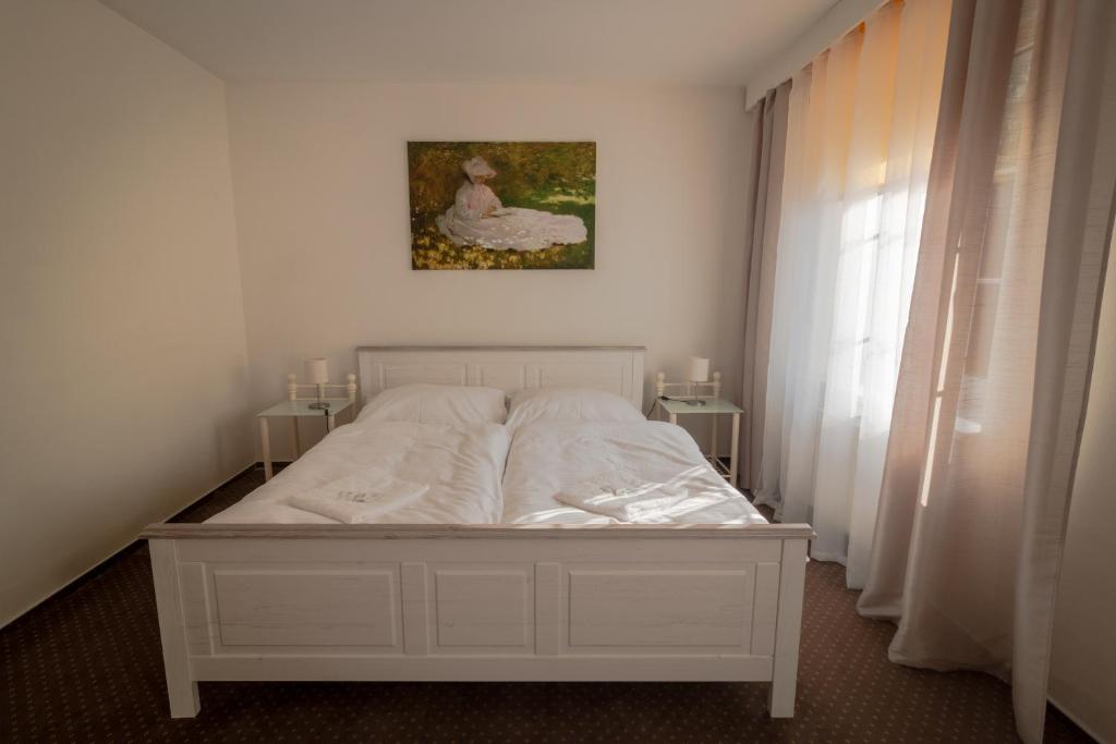 a bedroom with a white bed with a painting on the wall at Hotel Garni Orlova in Orlová