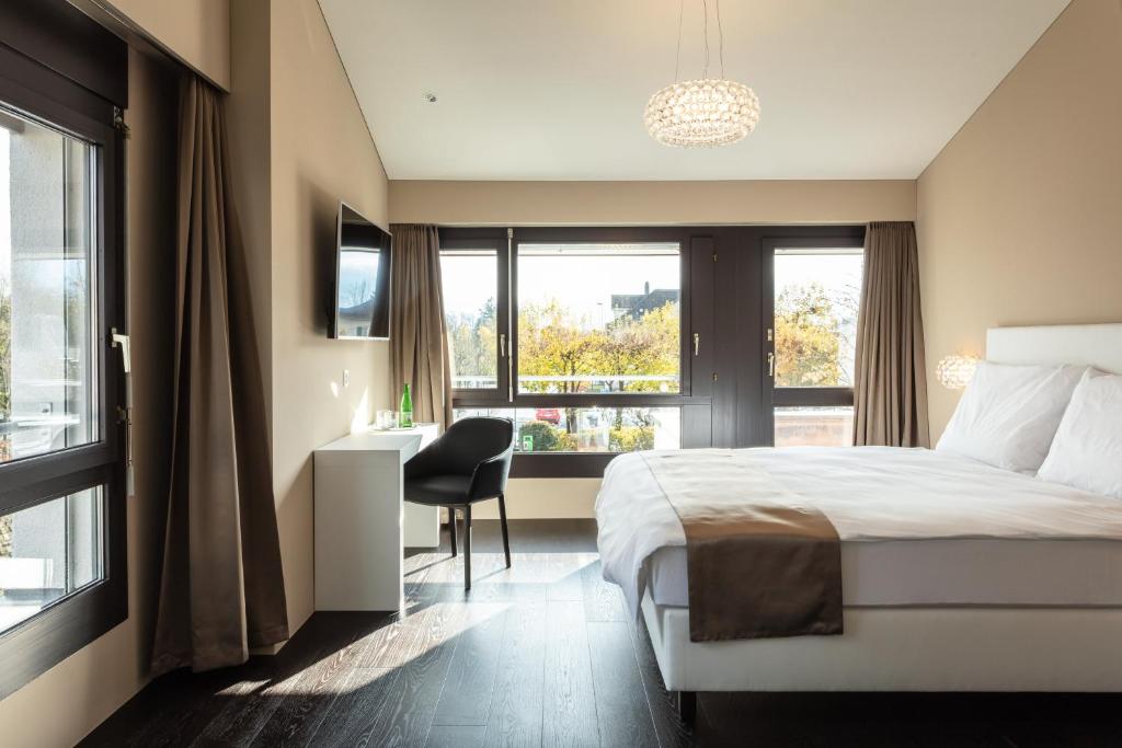 a bedroom with a bed and a desk and windows at Hotel Lo! im Kreuz Jona in Rapperswil-Jona