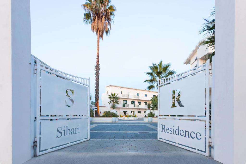 a gate to a resort with a palm tree in the background at Sibari Residence in Marina di Sibari