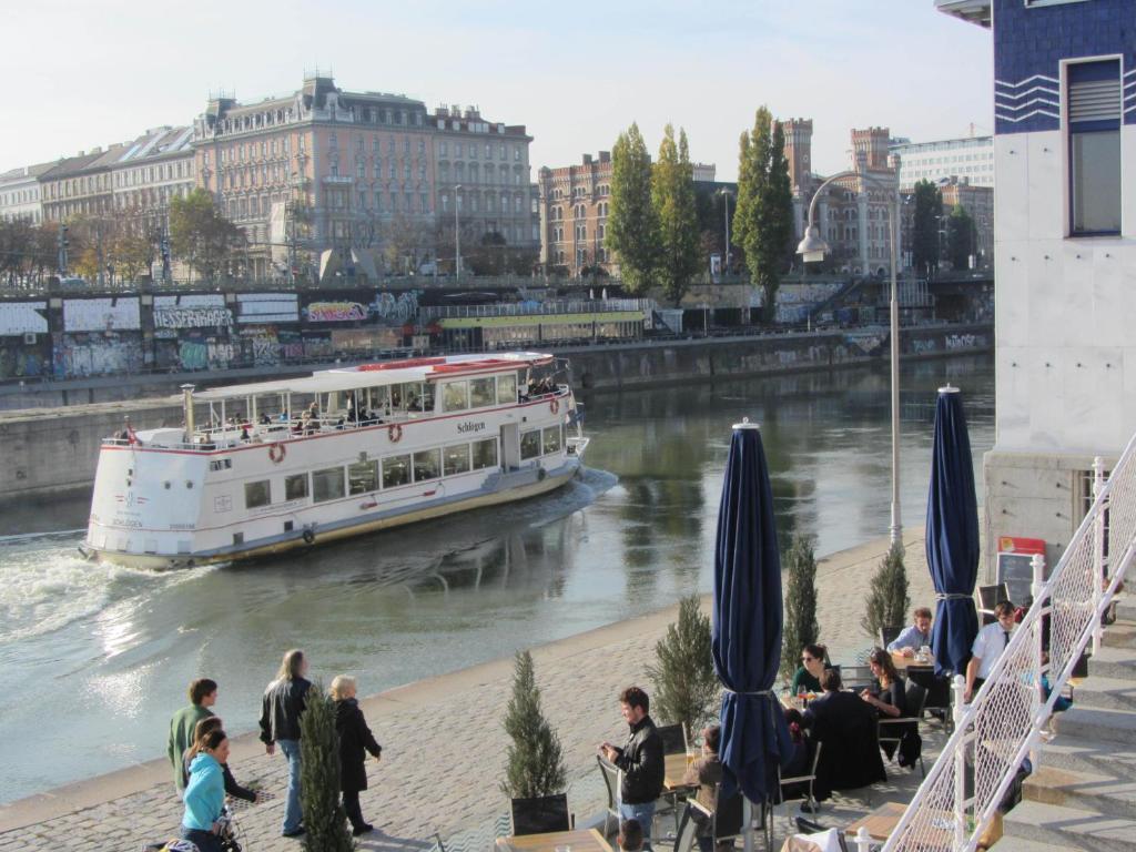 un barco que viaja río abajo con gente en la orilla en Wohnen im Herzen von Wien at the Waterfront en Viena