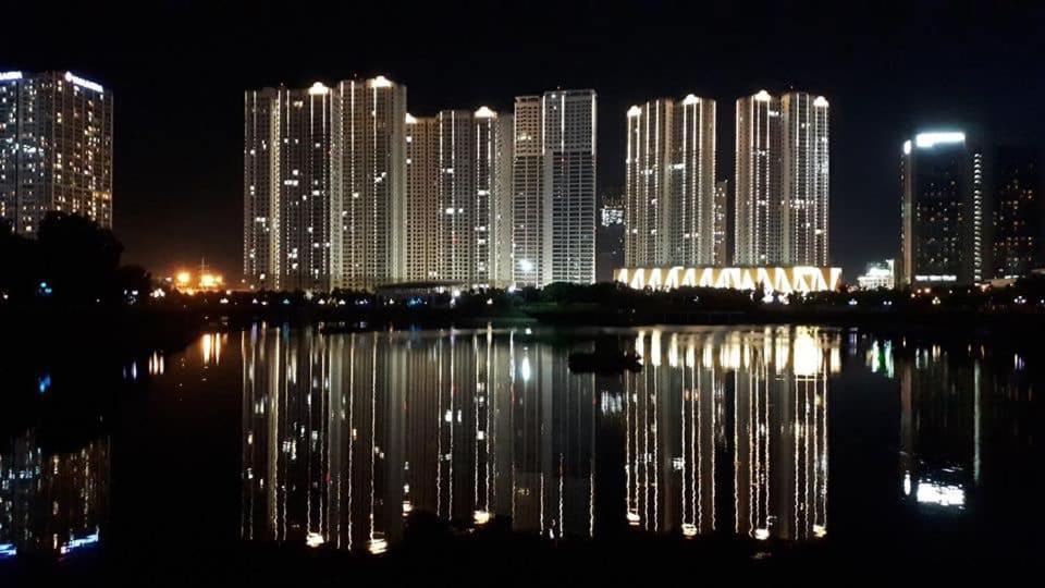 un grupo de edificios altos por la noche con un cuerpo de agua en Vinhomes D'Capitale Apartment - by Bayhomes, en Hanói