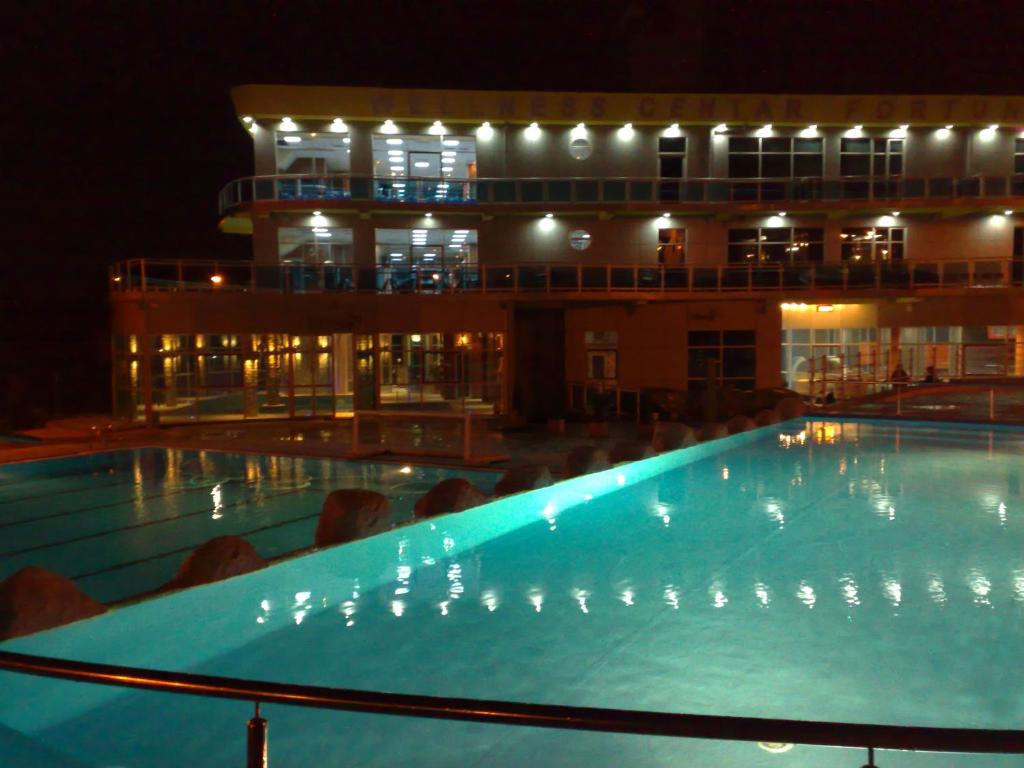 a large swimming pool in front of a building at night at Hotel Fortuna in Banja Luka