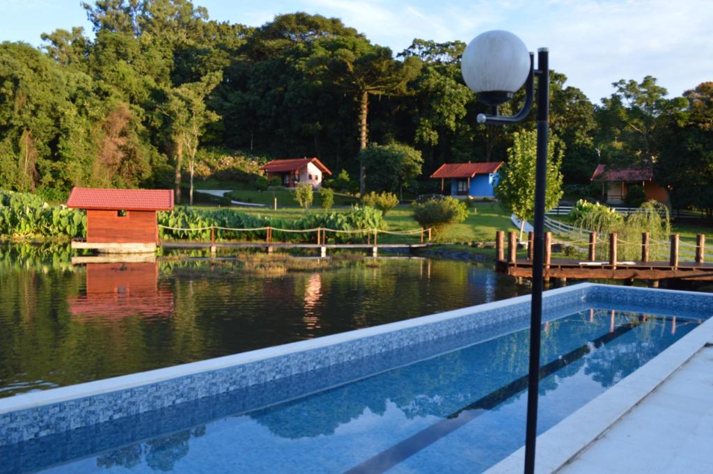 a swimming pool next to a lake with a house at Pousada Pinhal Alto in Nova Petrópolis