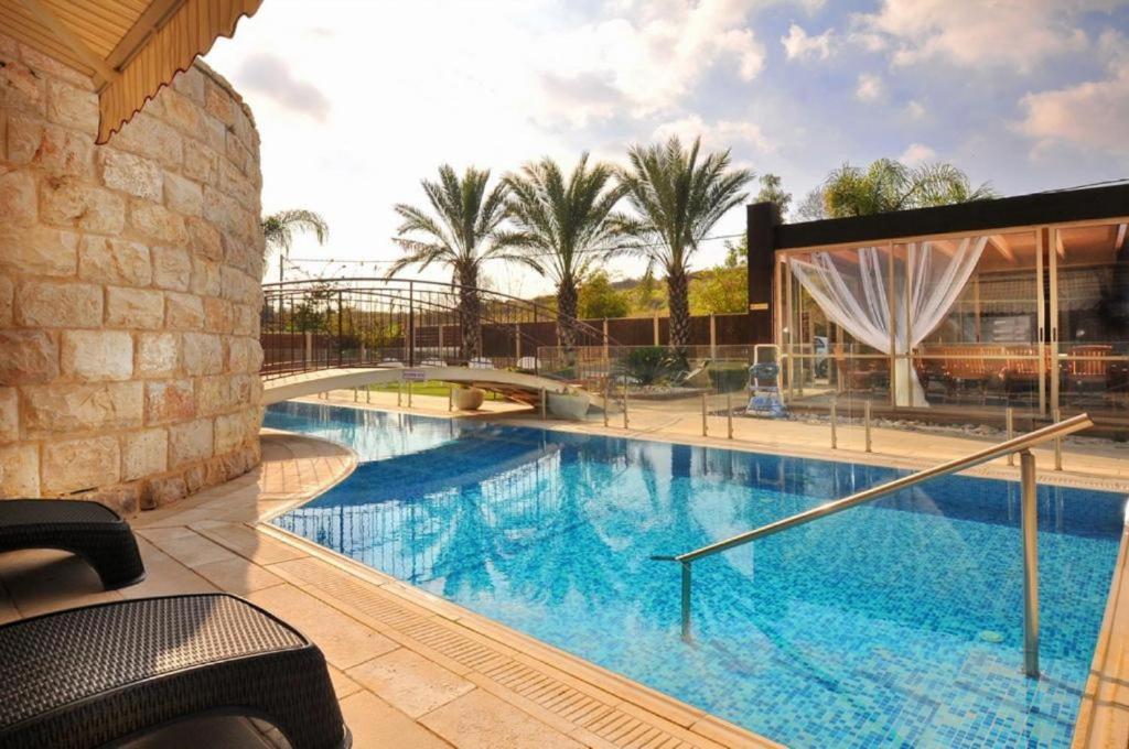 a large swimming pool with a bridge and palm trees at Ahuzat Elisheva in ‘Amqa