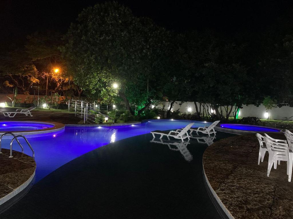 una piscina por la noche con sillas blancas alrededor en Apartamento moderno e totalmente acessível, en Pipa