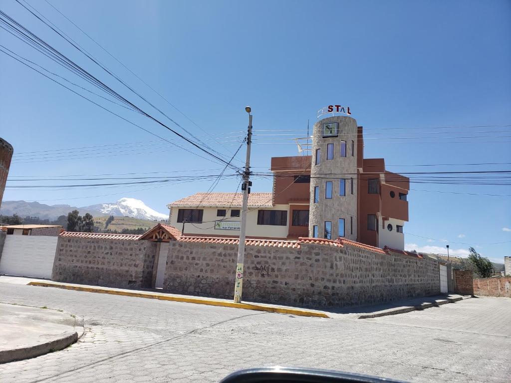 ein Gebäude mit einem Uhrturm neben einer Ziegelwand in der Unterkunft Hospedaje San Fernando in Cayambe