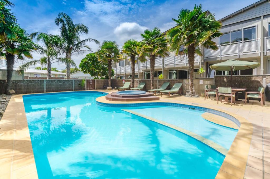 a swimming pool with palm trees and a building at Raumati Sands Resort in Paraparaumu Beach